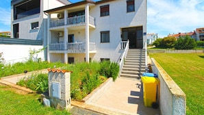Un immeuble résidentiel à plusieurs étages, doté de balcons, d’un escalier et d’un petit jardin.