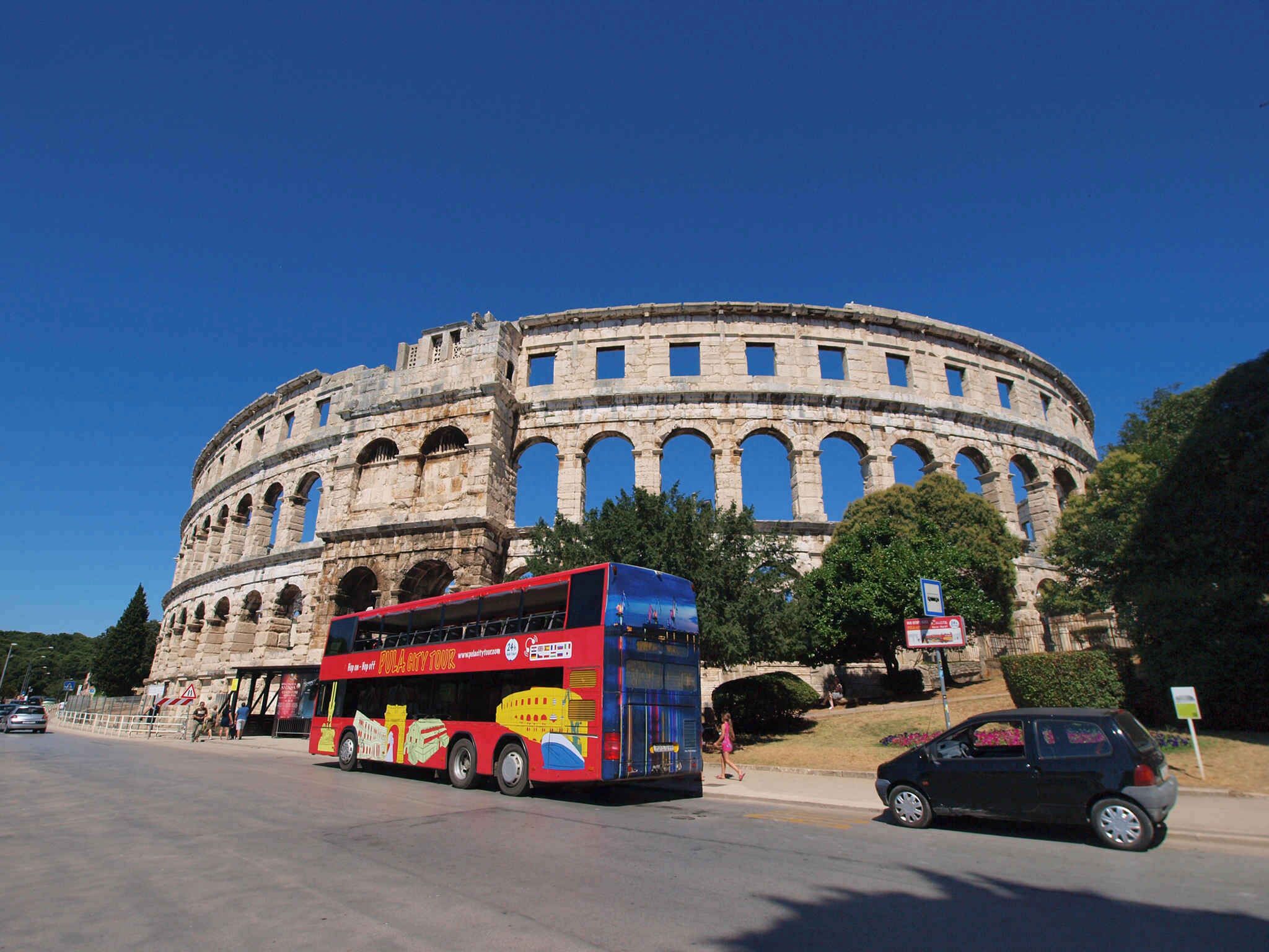 Un bâtiment historique doté de nombreuses arcades, devant lequel est garé un autobus à deux étages rouge.