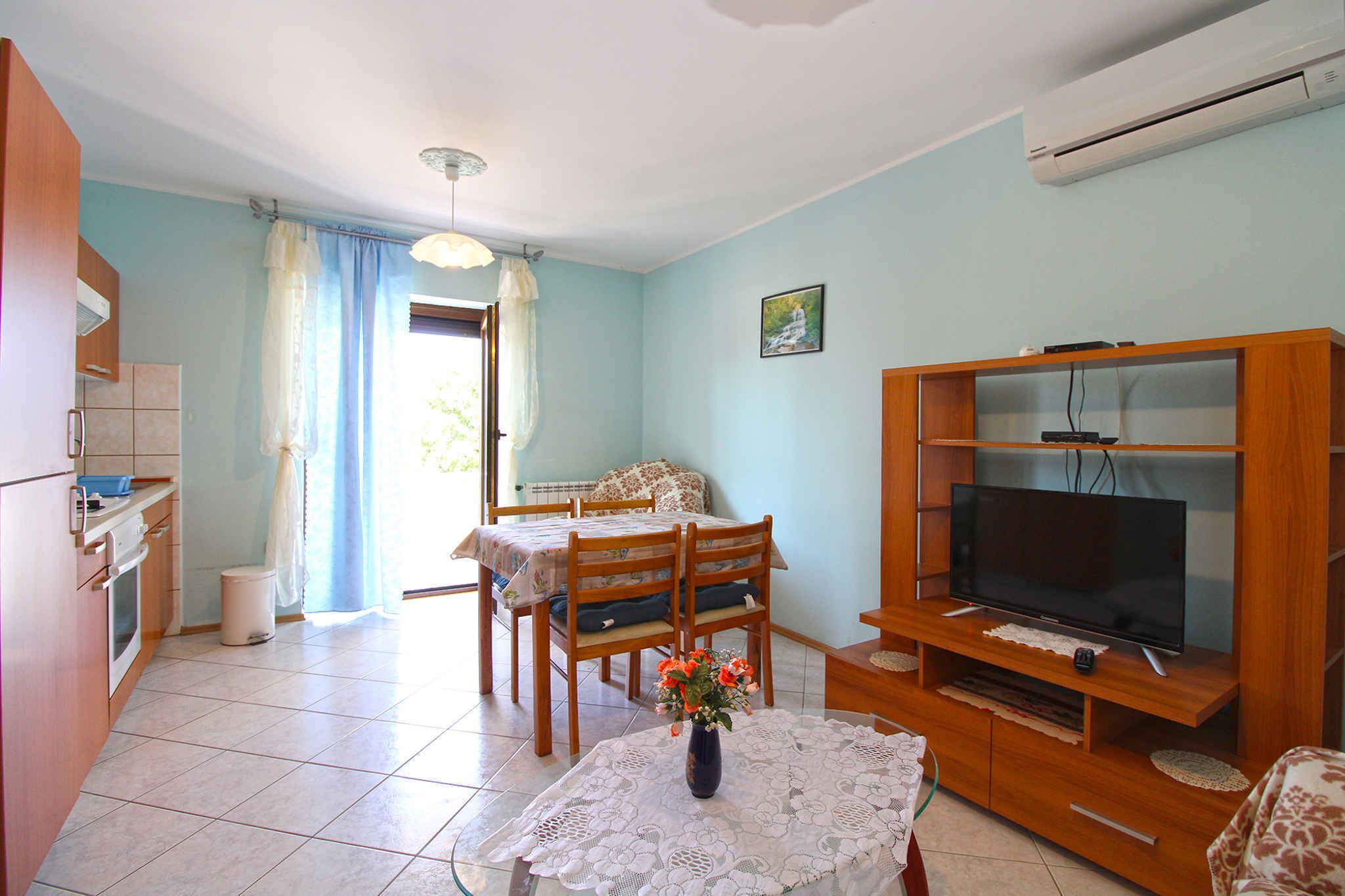 A living room with a dining area, a TV on a wooden stand, and a kitchen area with cabinets and a sink.