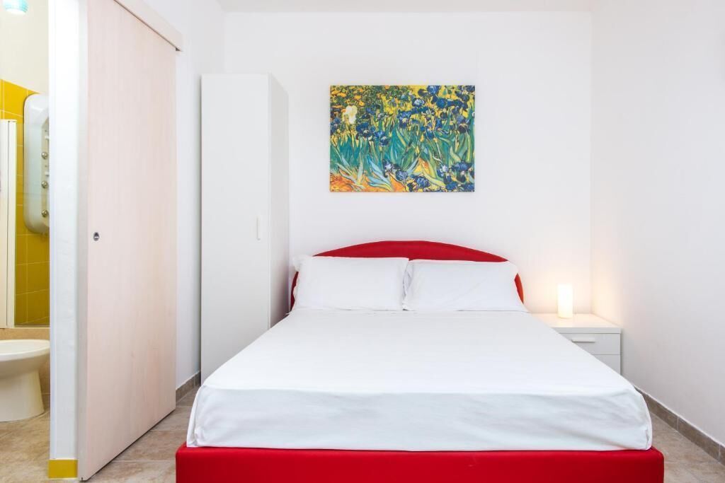 Hotellihuone, jossa on sänky, yöpöytä, seinällä taulu ja avoimesta ovesta näkyy kylpyhuone.