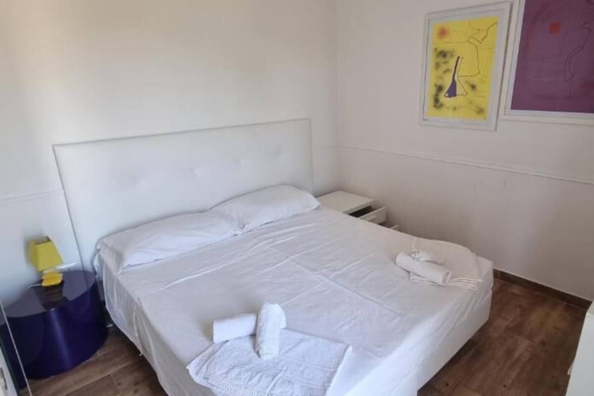 A hotel room with a bed, a nightstand, a lamp, and a small desk.