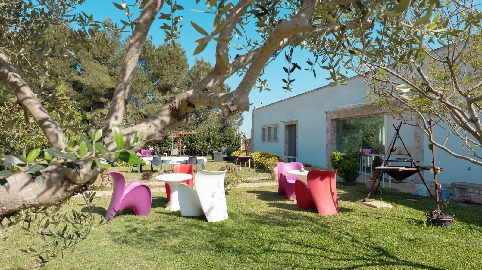 An outdoor seating area with various tables and chairs, surrounded by greenery and trees.