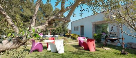 An outdoor seating area with various tables and chairs, surrounded by greenery and trees.