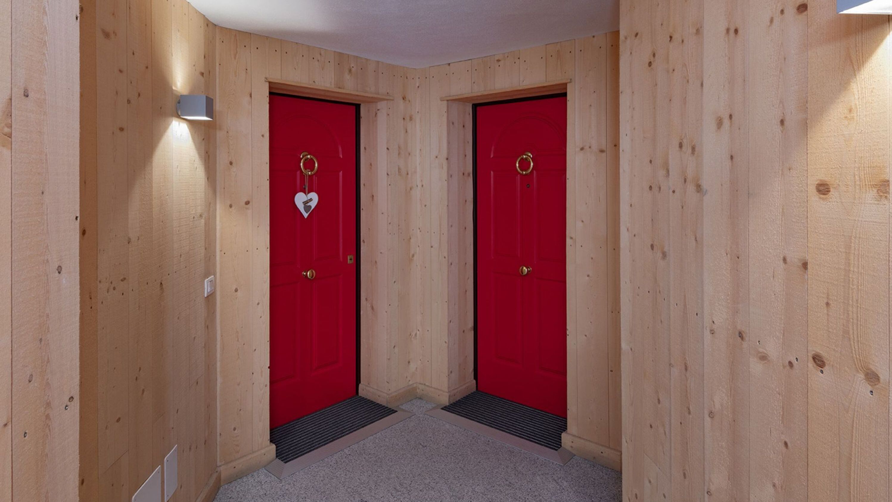 A hallway with two red doors, each with a heart-shaped decoration and a circular ring.
