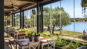 Un ristorante con ampie vetrate che si affacciano su un lago, tavoli in legno e piante pensili.