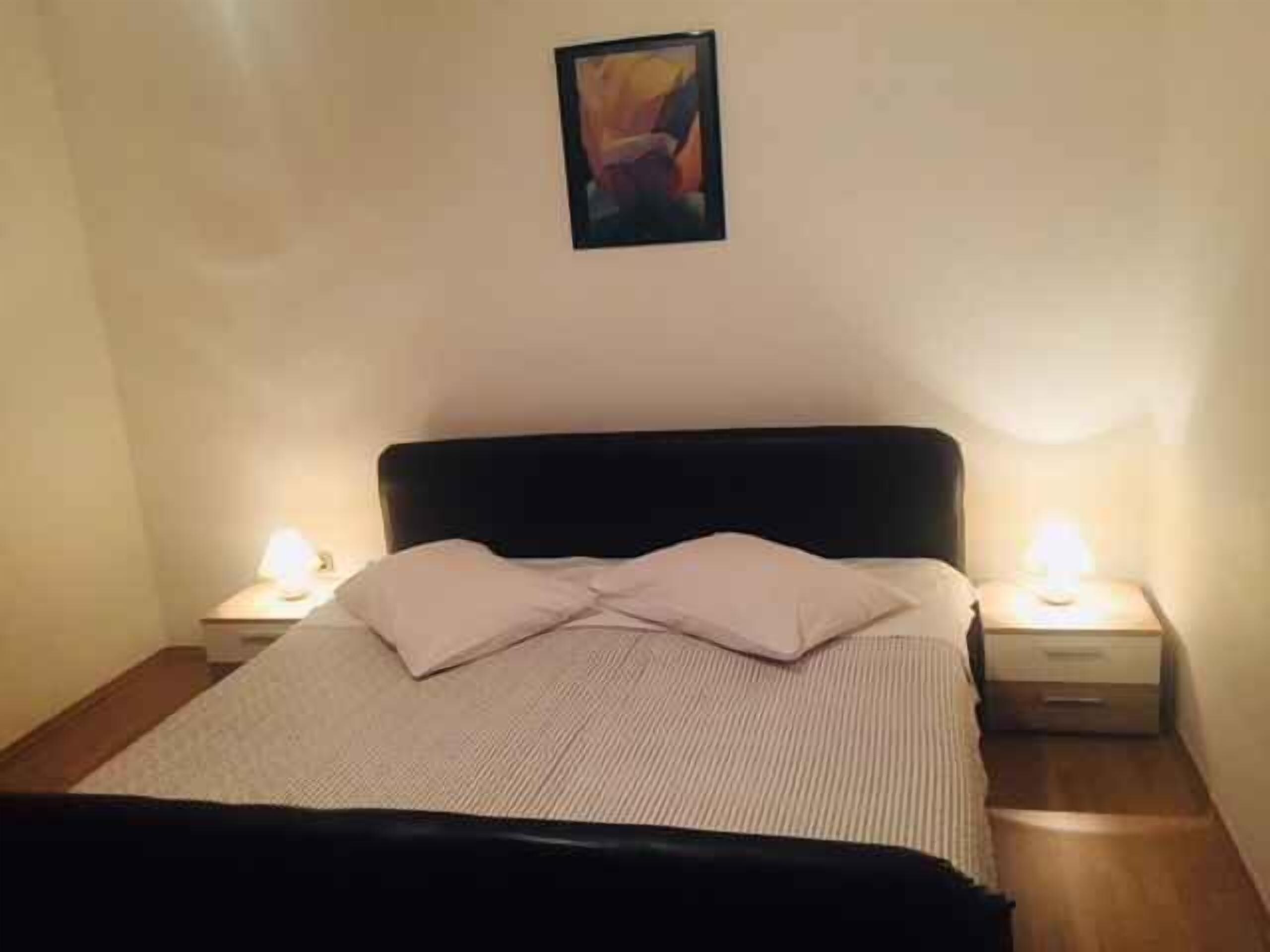 A neatly made bed with a black headboard, two bedside tables with lamps, and a framed picture on the wall.