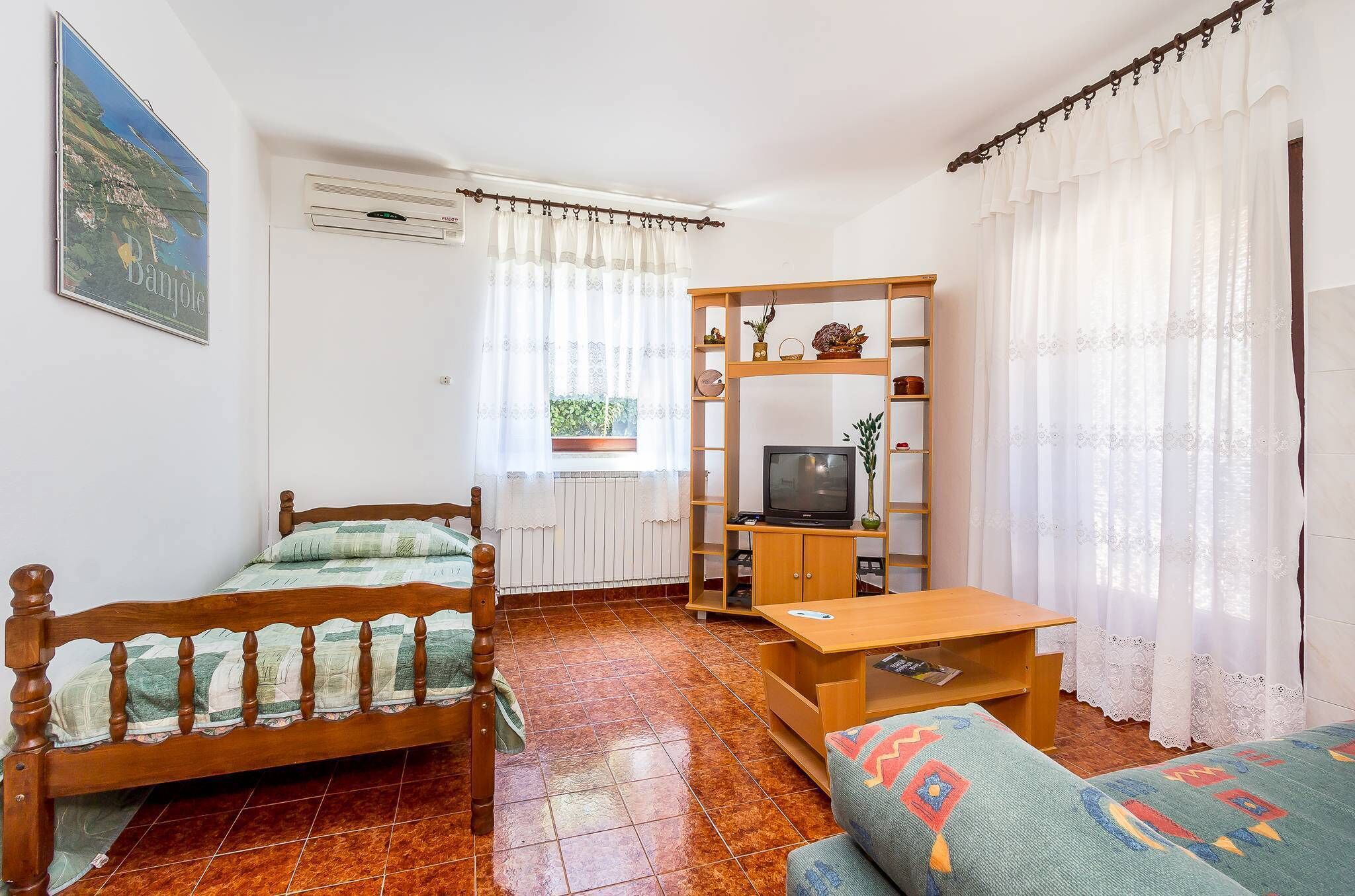 Una habitación con una cama, un televisor sobre un mueble de madera, un sofá y una ventana con cortinas.