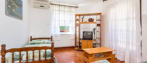 Una habitación con una cama, un televisor sobre un mueble de madera, un sofá y una ventana con cortinas.