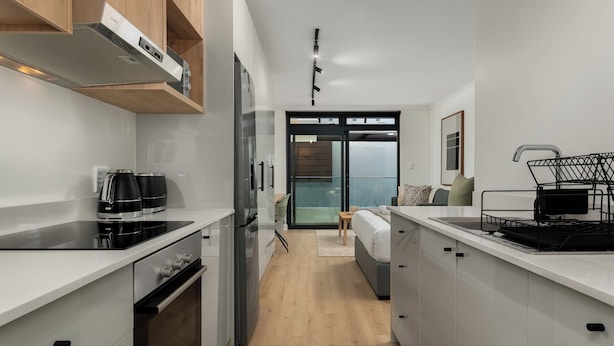 A modern kitchen with white cabinetry, a built-in oven, and a coffee maker. - The Sage | Studio With Courtyard Access (Cape Town)