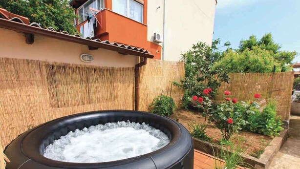 A hot tub filled with water, surrounded by a wooden fence and a garden with red flowers. - Holiday home with air conditioning (Pula)