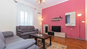 A living room with a sofa, a coffee table, a TV, and a pink wall. - Holiday home with air conditioning (Pula)
