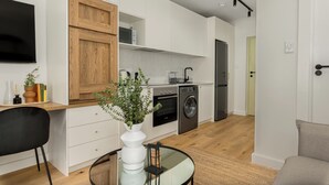 A modern kitchen with white cabinets, a wooden door, a washing machine, and a built-in oven.