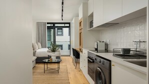 A compact kitchen with a washing machine, a dining area with a table and chairs, and a living room with a sofa and a plant.