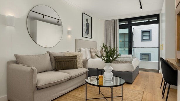 A modern living room with a sofa, a round coffee table, and a bed with a headboard.