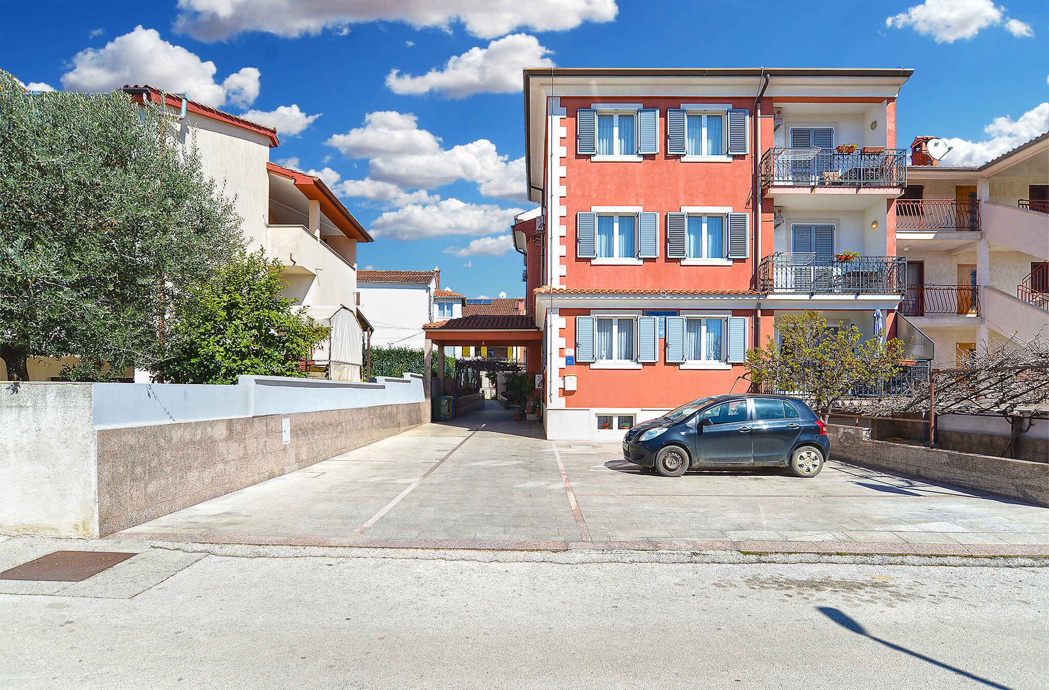 Un edificio residencial de varios pisos con balcones, un estacionamiento y cielo despejado.