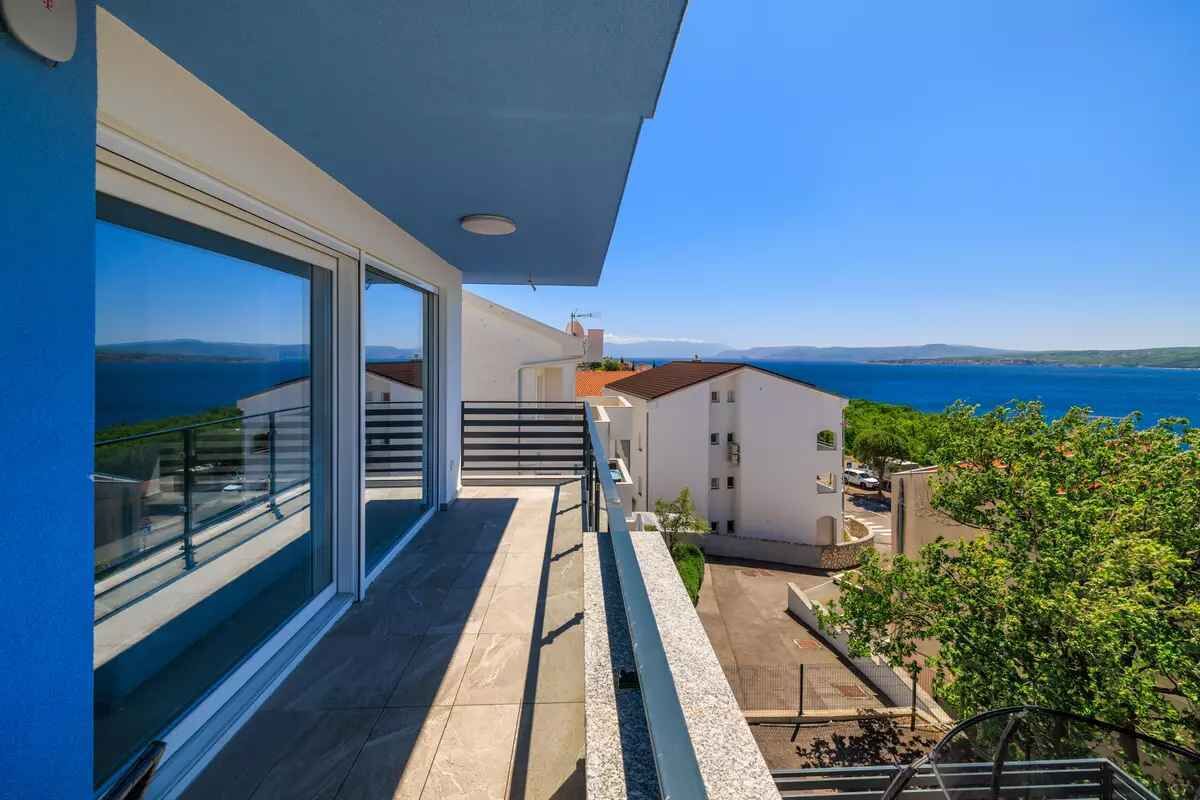 A balcony with a view of the sea, a clear sky, and a modern building with large windows.