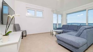 A modern living room with a grey sofa, a small round table, a white desk, and a potted plant. - Holiday apartment fully air-conditioned with balcony and sea view (Dramalj)