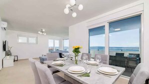 A modern dining area with a large table set for six, a view of the sea through large windows, and a balcony with a railing. - Holiday apartment fully air-conditioned with balcony and sea view (Dramalj)