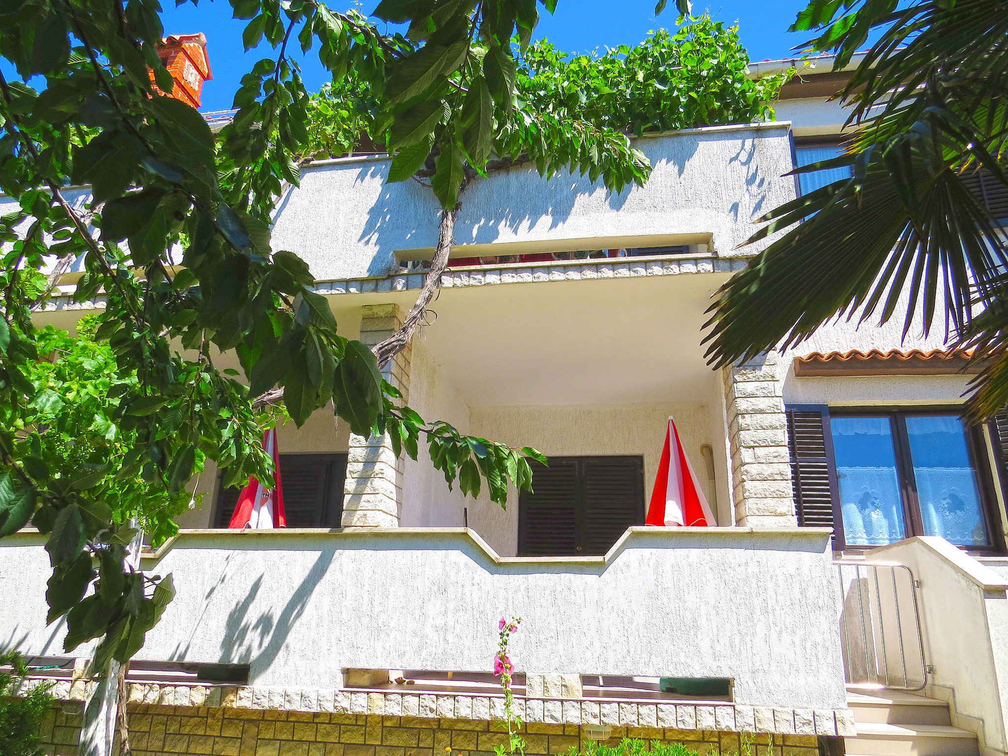 A two-story building with a balcony, a stone wall, and a palm tree in the foreground.