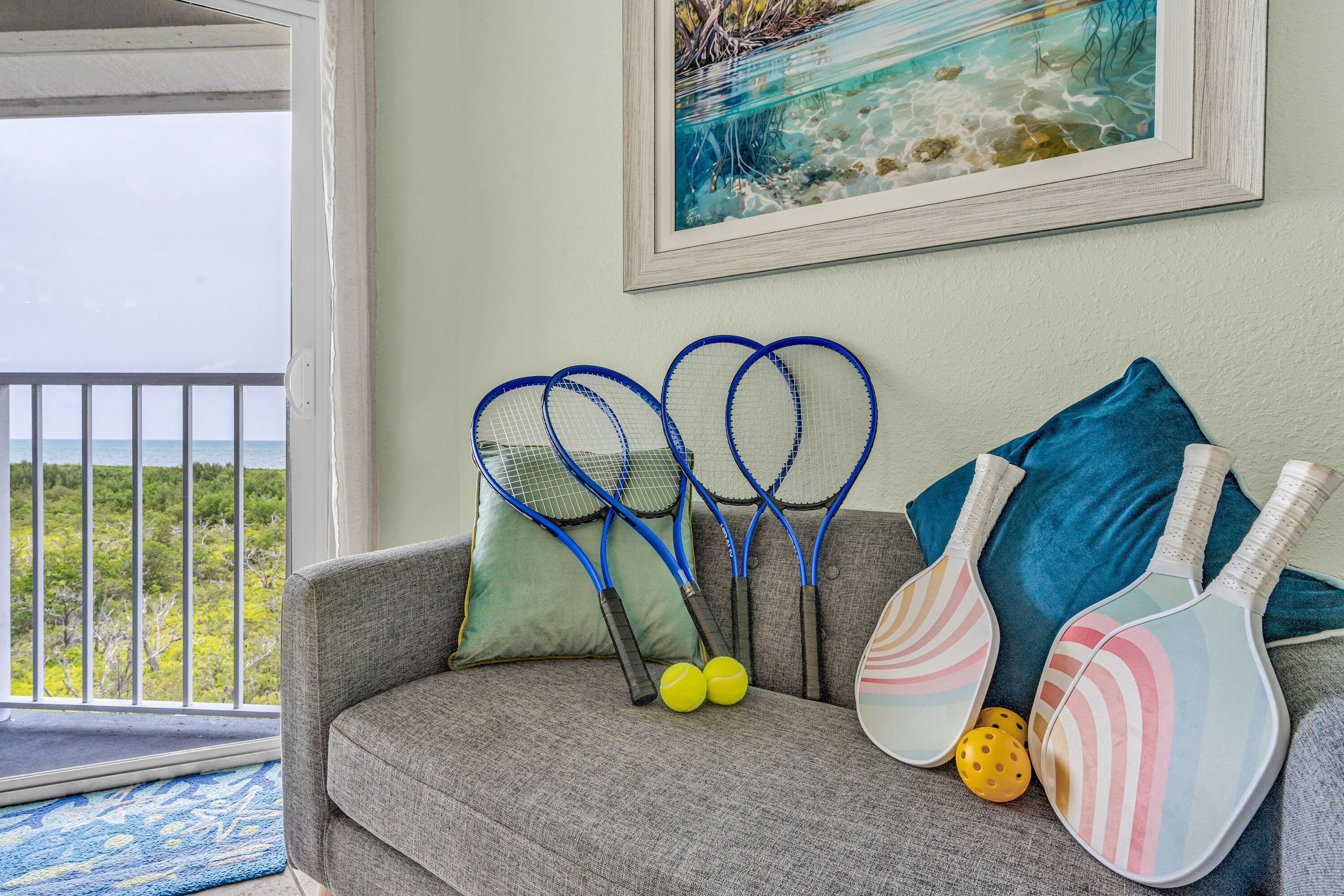 A room with a grey sofa, tennis rackets, and two tennis balls.