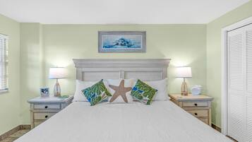 A neatly made bed with a starfish pillow, two nightstands with lamps, a framed picture above the bed, and a closed door on the right.
