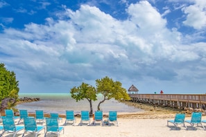 A beach with turquoise chairs, a wooden pier, and a thatched-roof structure.