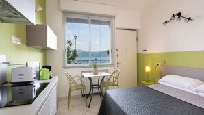 Habitación de hotel compacta con cama, kitchenette pequeña, zona de comedor con mesa y sillas, y ventana con vistas.