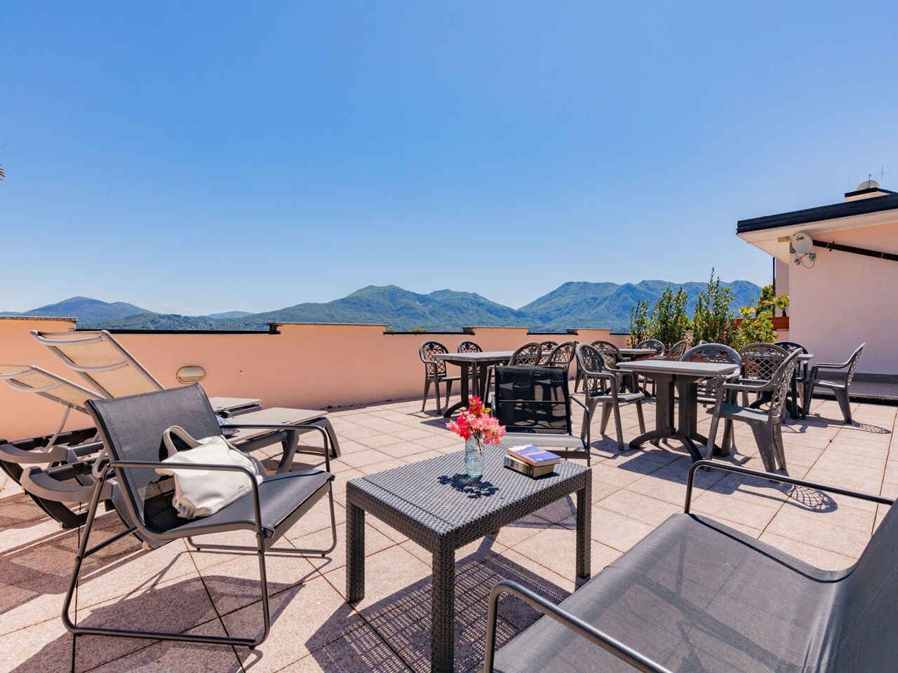 A rooftop terrace with outdoor furniture, a table with a vase of flowers, and a view of distant mountains.