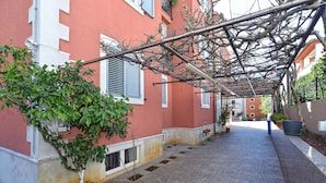 A narrow alleyway with a covered walkway, potted plants, and a building with shutters.