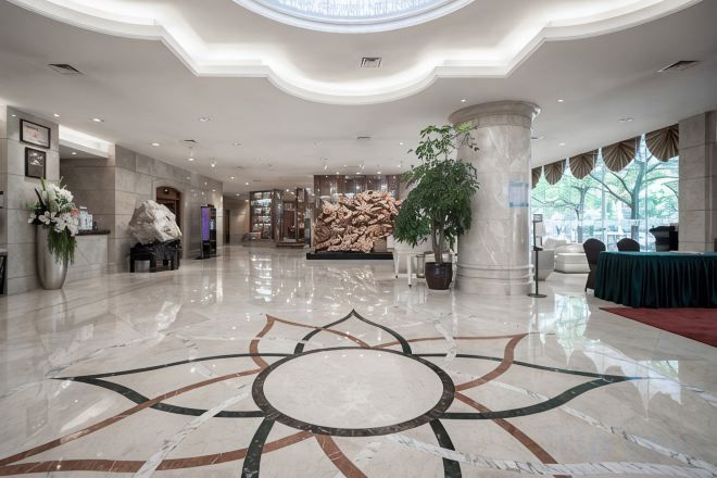 A hotel lobby with a polished marble floor, a reception desk, and a large potted plant.