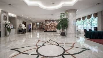 A hotel lobby with a polished marble floor, a reception desk, and a large potted plant.