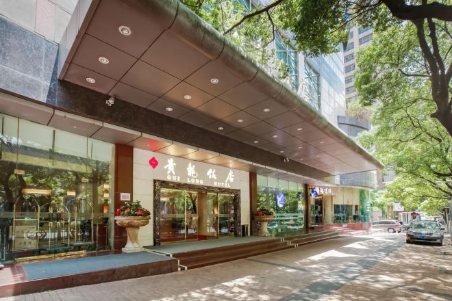 A hotel entrance with a glass facade, a red sign, and a staircase leading to the entrance.