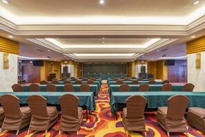 A conference room with rows of tables and chairs, a carpeted floor, and a stage at the front. - Guilong Hotel (Guiyang)
