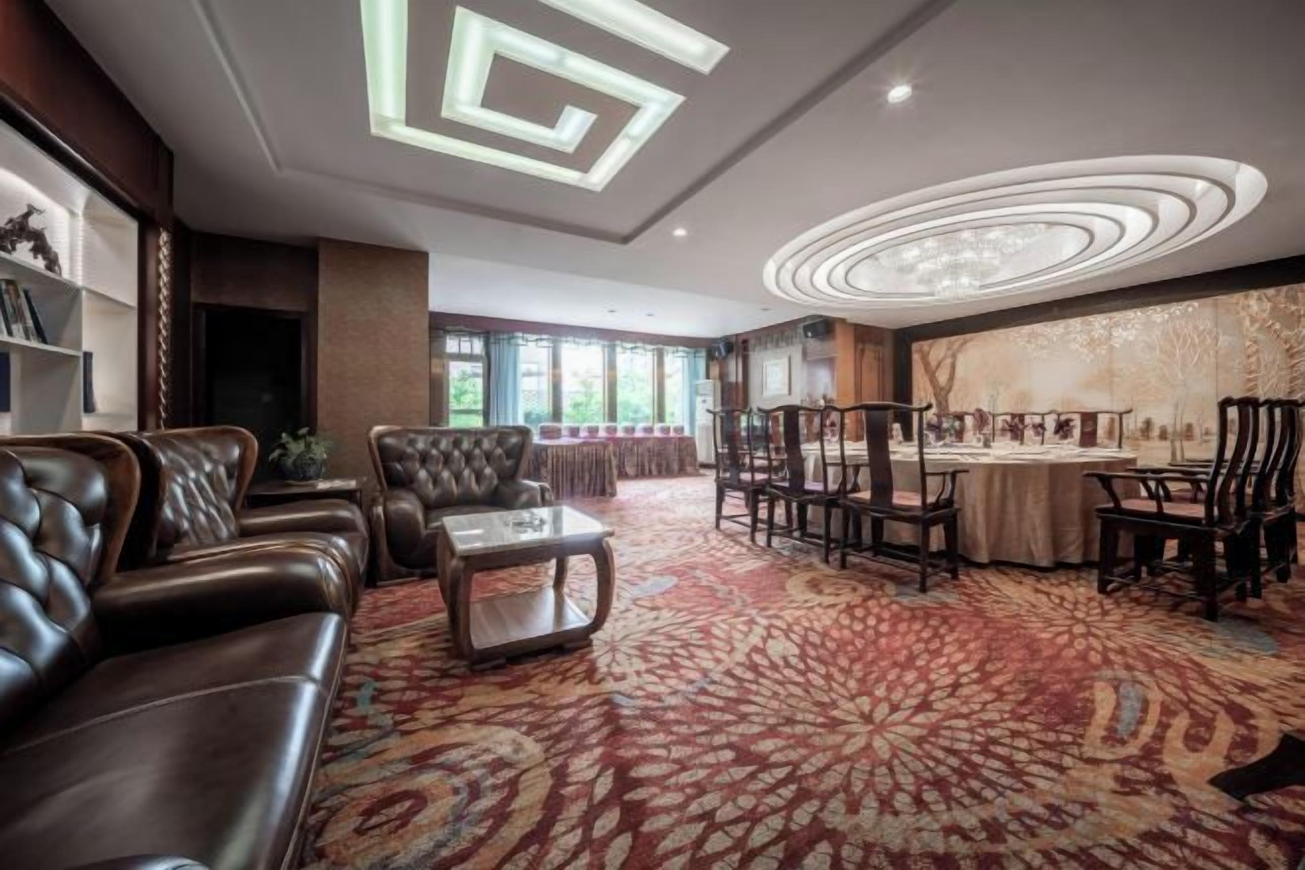 A spacious living room with a patterned carpet, leather sofas, a coffee table, and a dining area with chairs and a table.