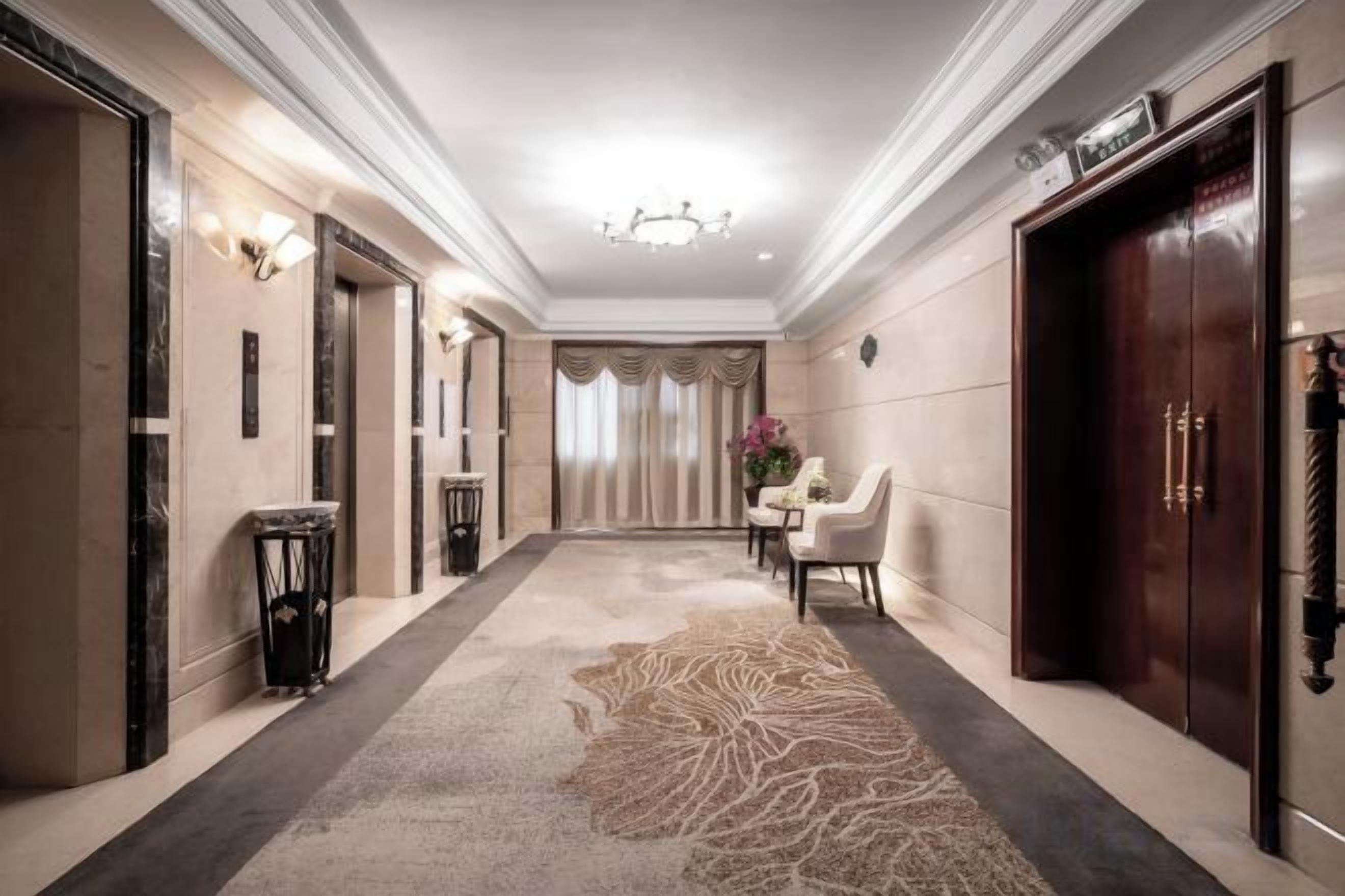 Un pasillo de hotel con alfombra, una lámpara de araña, un área de comedor y una recepción.
