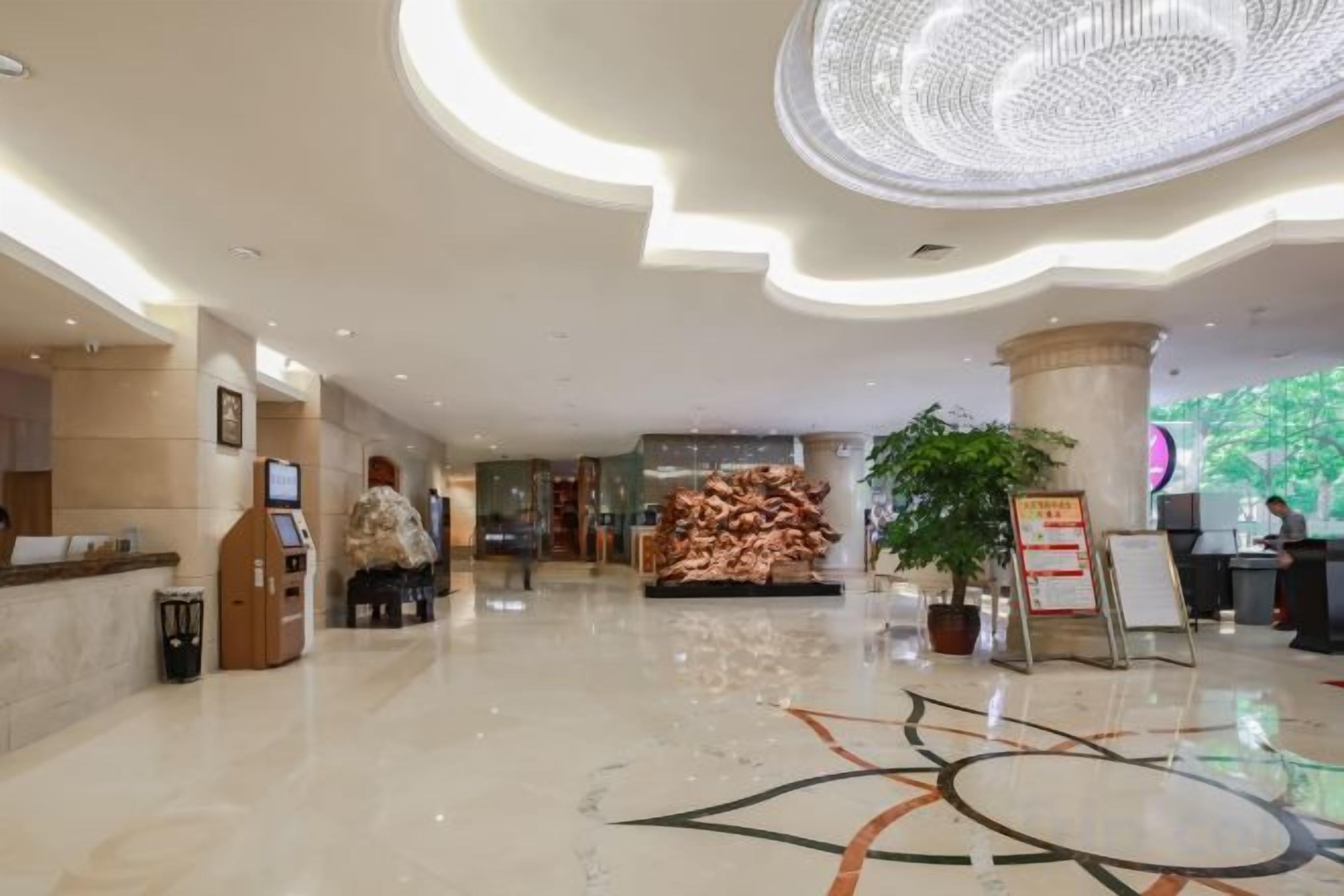 En hotellobby med en receptionsdisk, en stor, dekorativ taklampa och en centralt placerad växt.