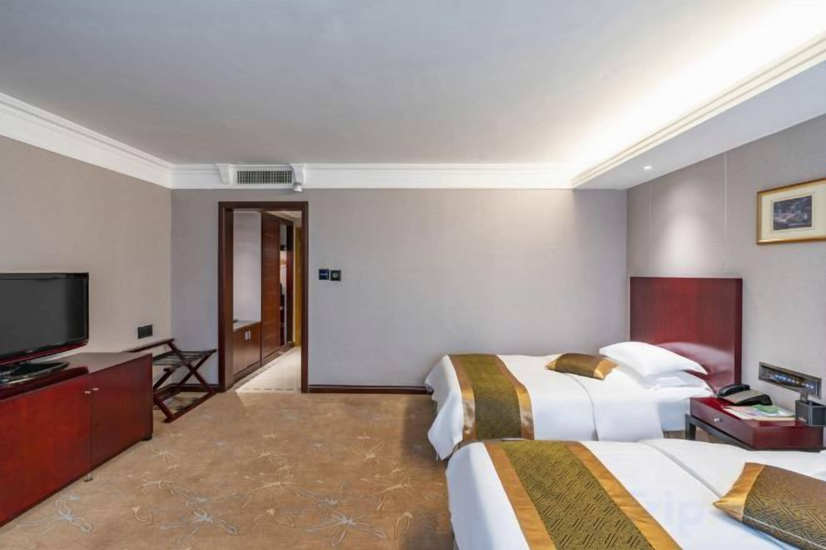 A hotel room with a television, a desk, two beds, and a door leading to another room.