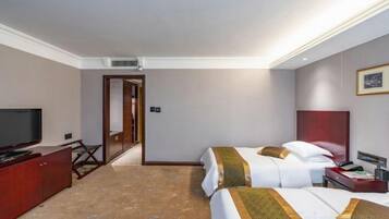 A hotel room with a television, a desk, two beds, and a door leading to another room.