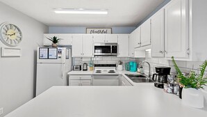 Una cocina moderna con armarios blancos, un reloj, un microondas, una estufa y una cafetera.