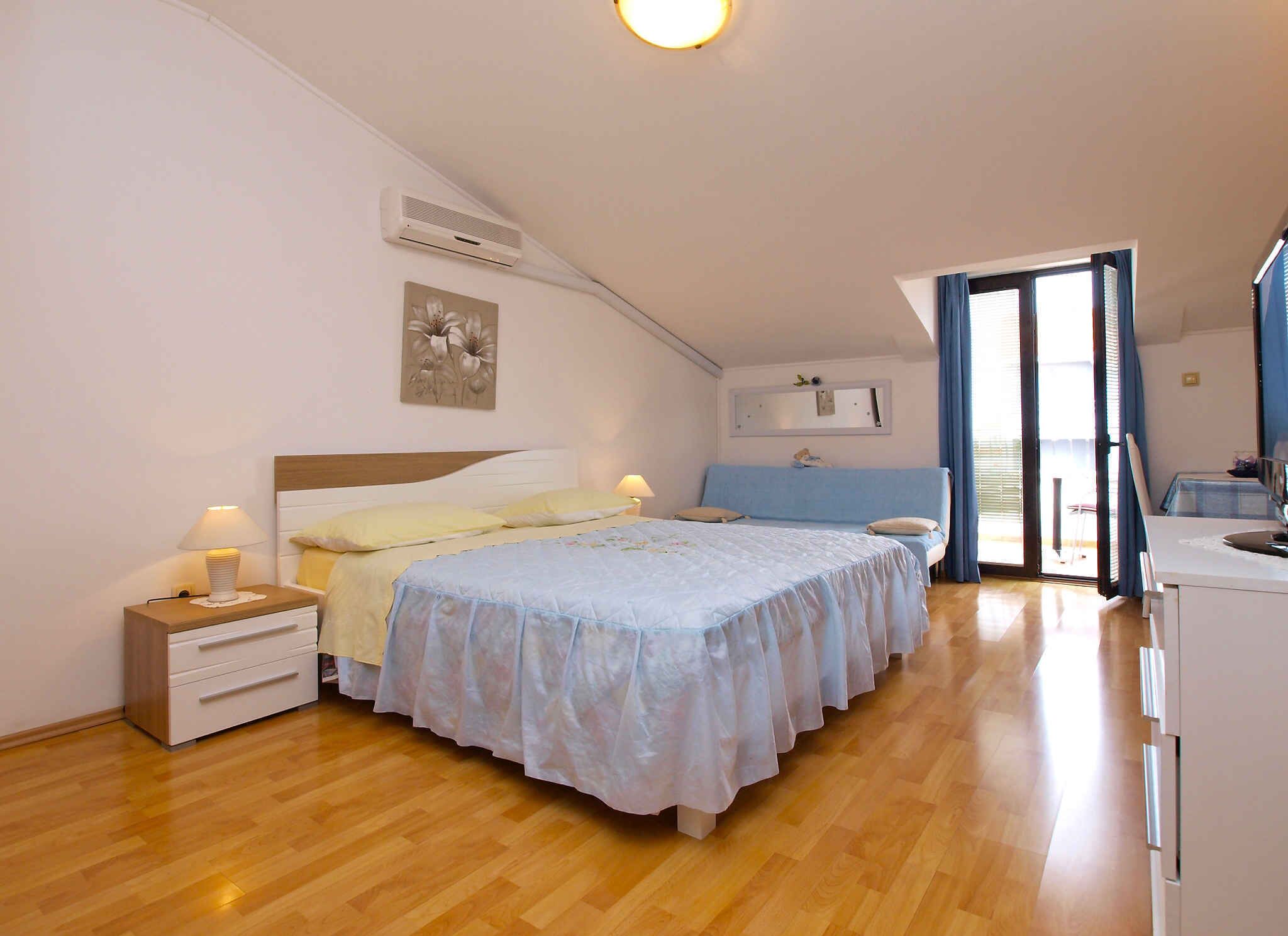 Un dormitorio con cama, mesitas de noche, escritorio, silla, ventana y puerta.