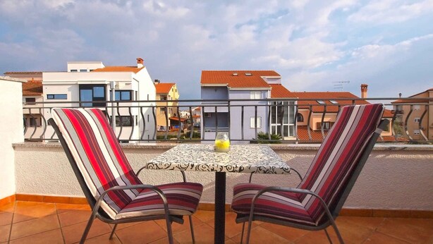 A terrace with two striped chairs and a small table, overlooking a residential area with modern and traditional buildings. - Studio with air conditioning and balcony (Rovinj)