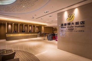 Ein Hotel-Rezeptionsbereich mit modernem Design, einem Empfangstresen und einer Wand mit dem Namen und dem Logo des Hotels.