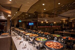 Un área de bufé con varias estaciones de comida, mesas y sillas.