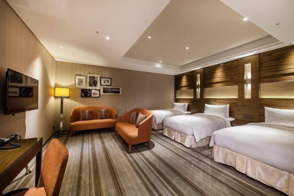 A hotel room with two beds, a sofa, a desk, and a TV.