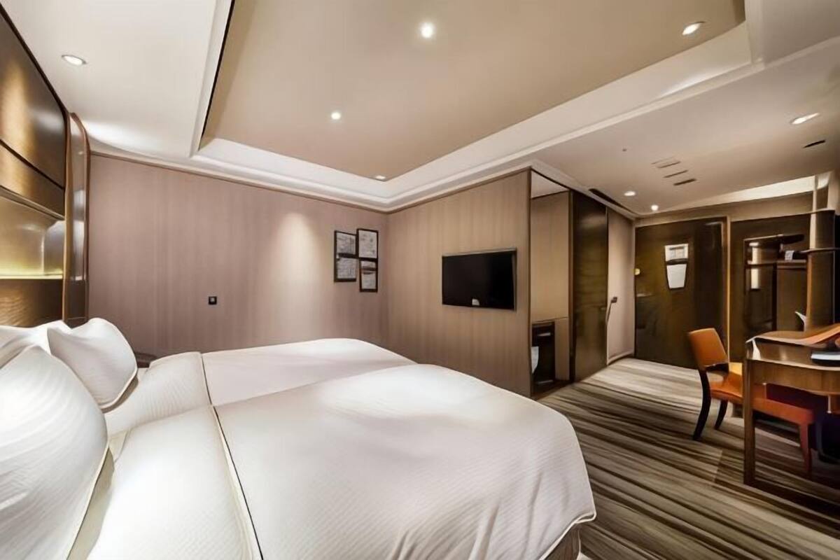A hotel room with a large bed, a desk, a chair, a TV, and a mirror.