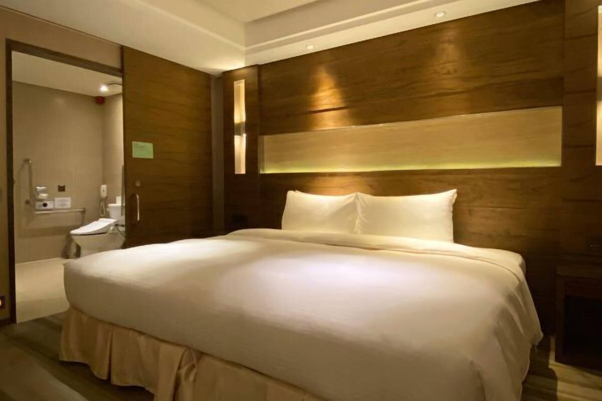 A hotel room with a large bed, wooden headboard, and a small bedside table.