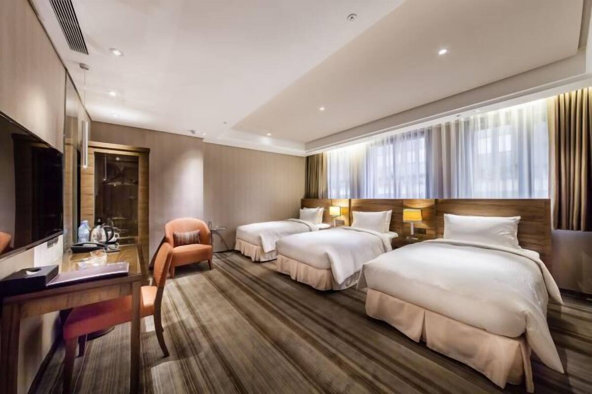 A hotel room with two beds, a desk, a chair, a TV, and a large window with curtains.