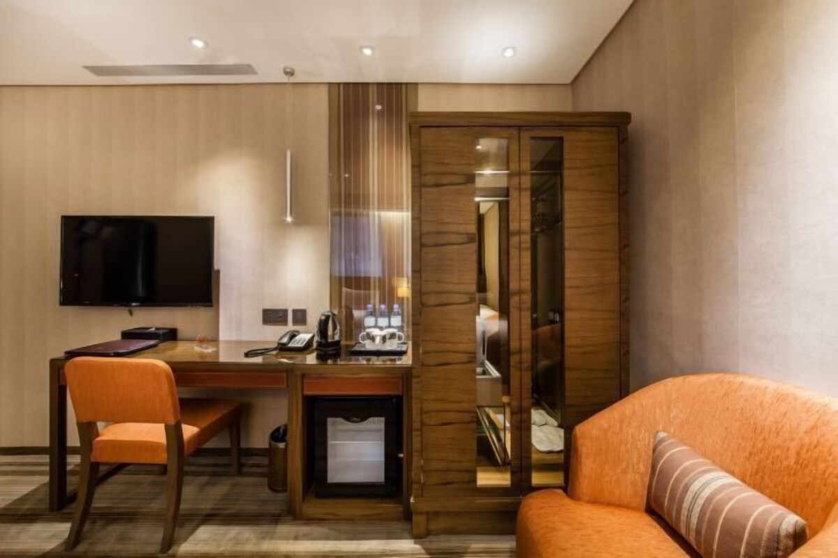 Quarto de hotel com escrivaninha de madeira, televisão, sofá e guarda-roupa com espelho.