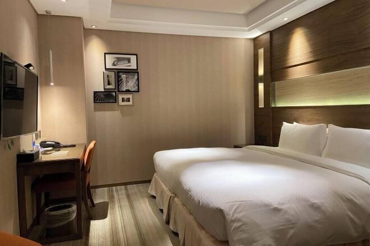 A hotel room with a bed, a desk, a chair, and a TV.