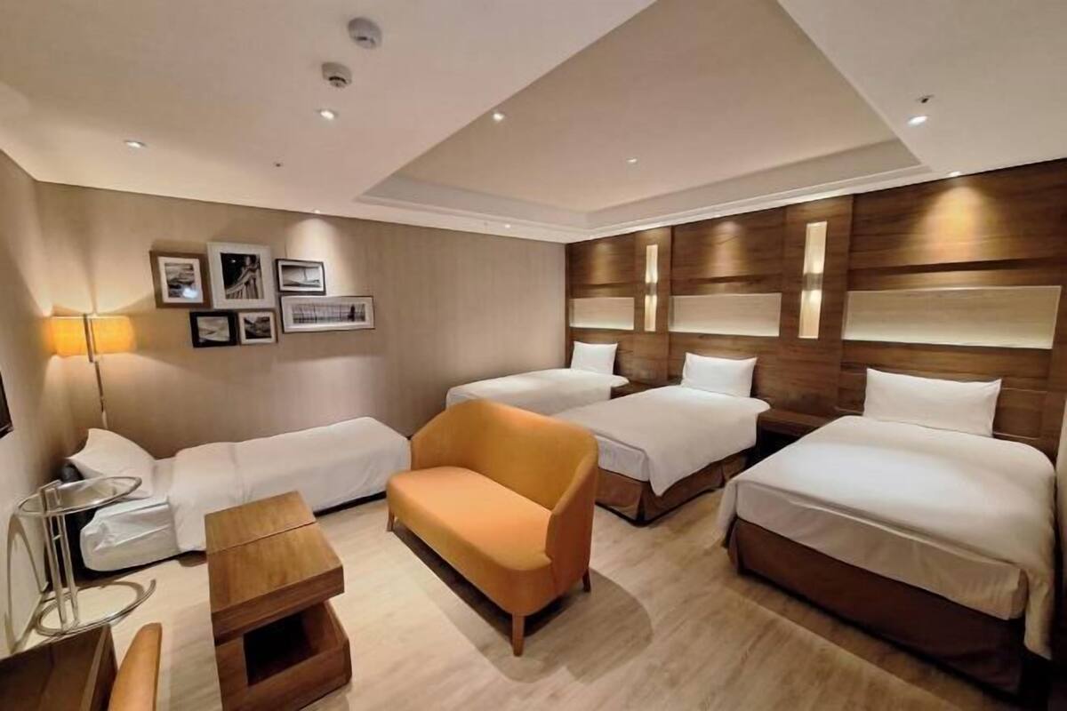 A hotel room with three beds, a sofa, a side table, and a lamp.